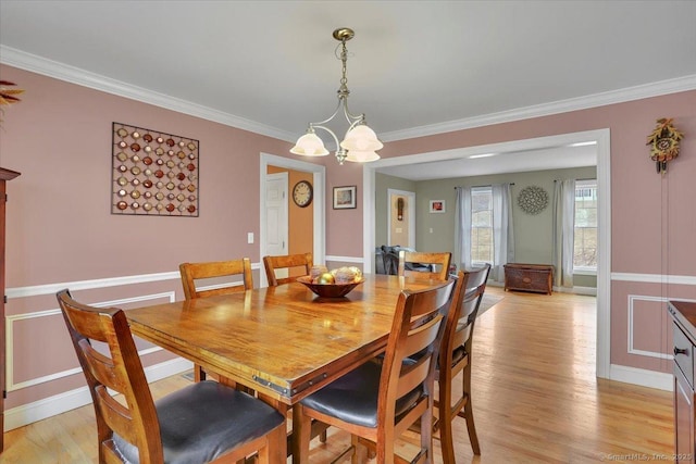 dining area with a notable chandelier, light wood-style floors, baseboards, and ornamental molding