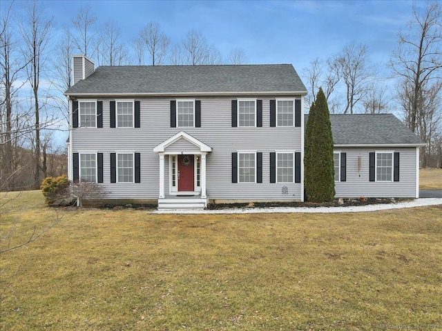 colonial house with roof with shingles, a chimney, and a front lawn