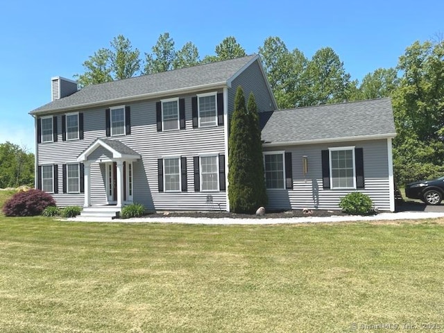 colonial house with a shingled roof, a front lawn, and a chimney