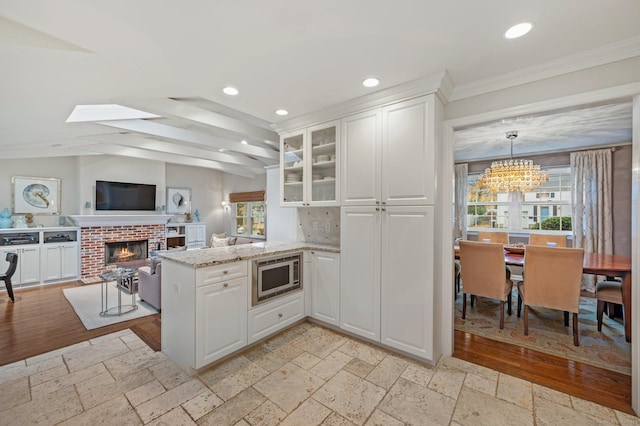 24 Laforge Rd, Darien, CT 06820 - kitchen featuring stainless steel microwave, a peninsula, a chandelier, a fireplace, and white cabinets