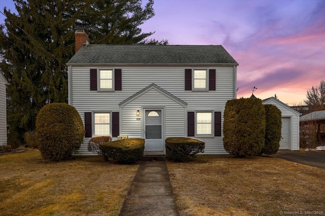 colonial inspired home with a garage, a chimney, a front yard, and a shingled roof