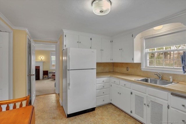 kitchen featuring white cabinets, ornamental molding, freestanding refrigerator, and a sink