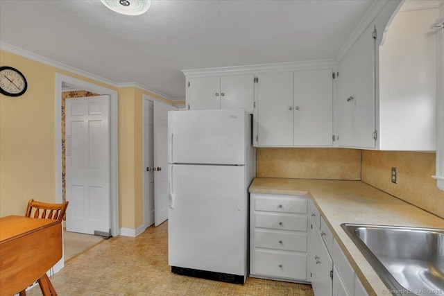 kitchen featuring freestanding refrigerator, ornamental molding, a sink, light countertops, and white cabinets