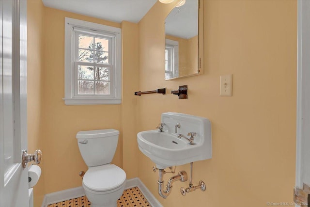 half bathroom with toilet, baseboards, and a sink