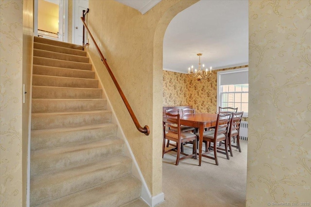 stairway featuring wallpapered walls, carpet flooring, arched walkways, and a chandelier