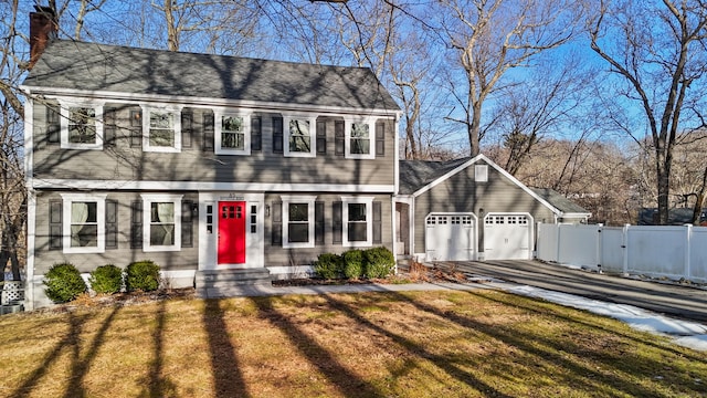 colonial-style house featuring an attached garage, a chimney, fence, and a front lawn