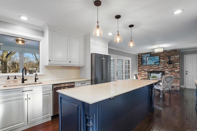 kitchen with appliances with stainless steel finishes, crown molding, a fireplace, white cabinetry, and a sink