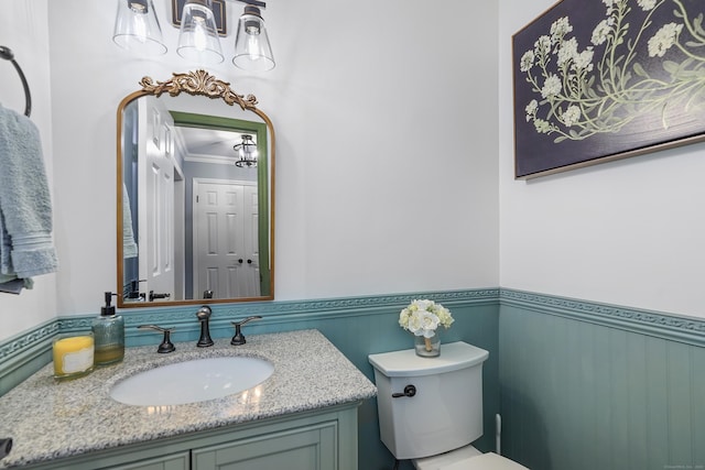 half bath featuring ornamental molding, a wainscoted wall, vanity, and toilet