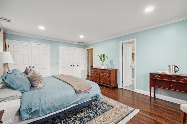 bedroom featuring baseboards, visible vents, wood finished floors, crown molding, and multiple closets