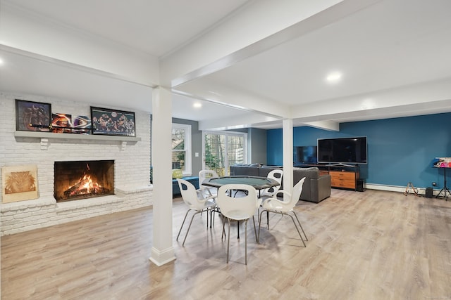 dining room with a brick fireplace, beamed ceiling, baseboards, and wood finished floors