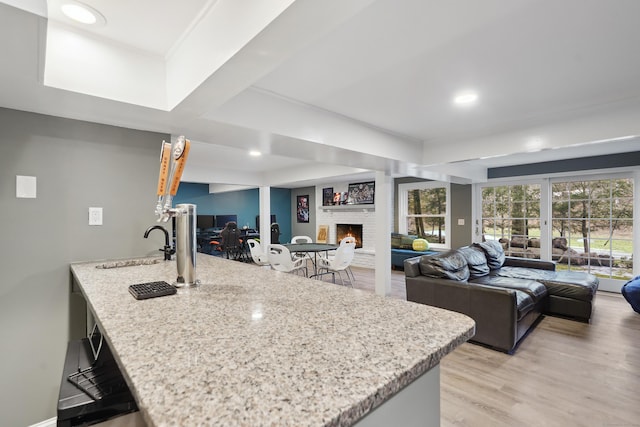 kitchen with light wood-style floors, open floor plan, a fireplace, and light stone countertops