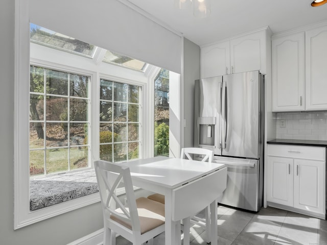 kitchen featuring dark countertops, backsplash, stainless steel fridge with ice dispenser, light tile patterned flooring, and white cabinetry