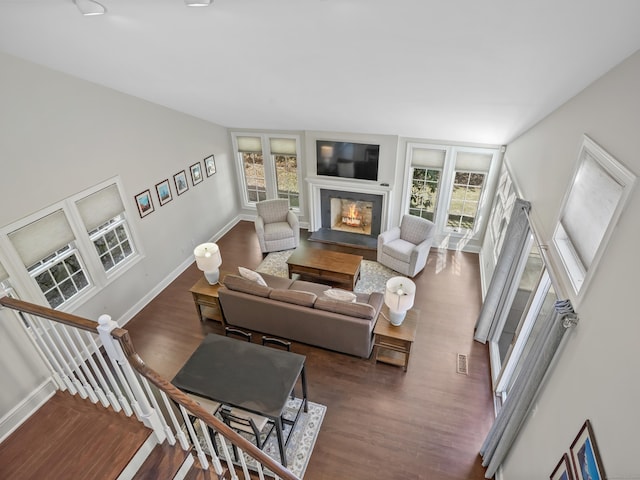 living area with dark wood-style floors, a glass covered fireplace, visible vents, and baseboards