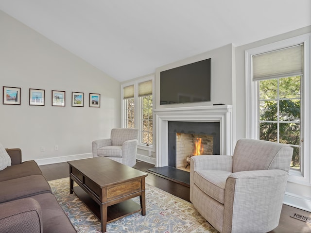 living room featuring wood finished floors, baseboards, visible vents, lofted ceiling, and a lit fireplace