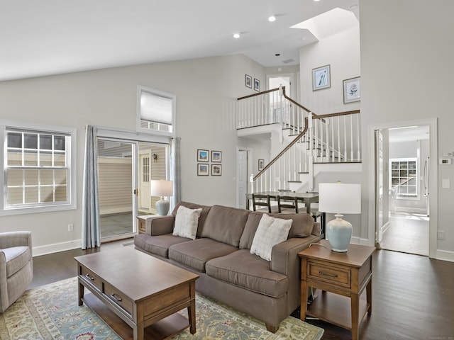 living room featuring stairway, wood finished floors, baseboards, high vaulted ceiling, and a skylight