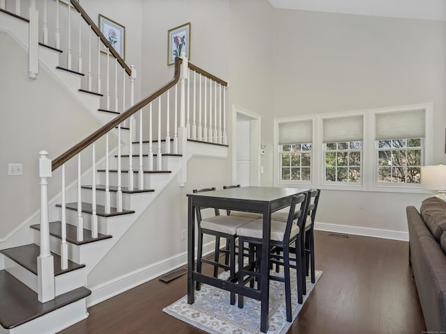 dining space featuring a towering ceiling, stairway, baseboards, and wood finished floors