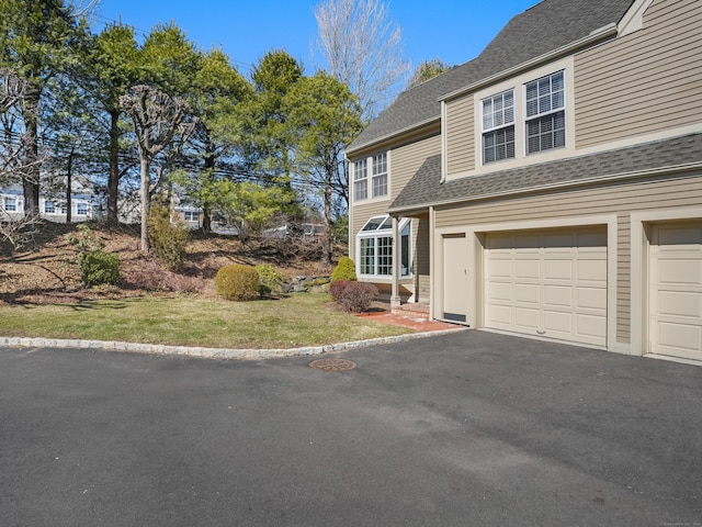 view of front of house with a garage, driveway, a front lawn, and roof with shingles