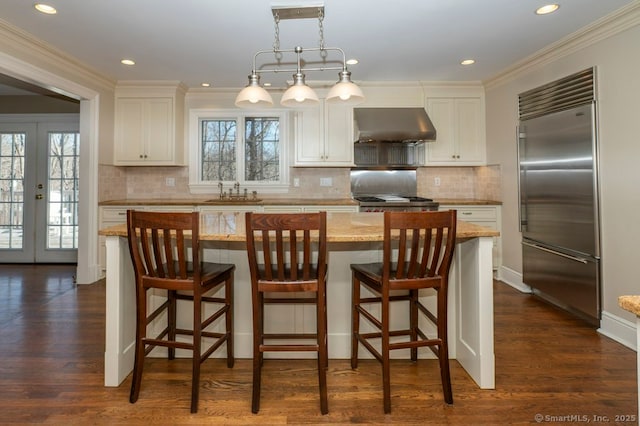 kitchen with dark wood-style flooring, white cabinets, built in fridge, and under cabinet range hood