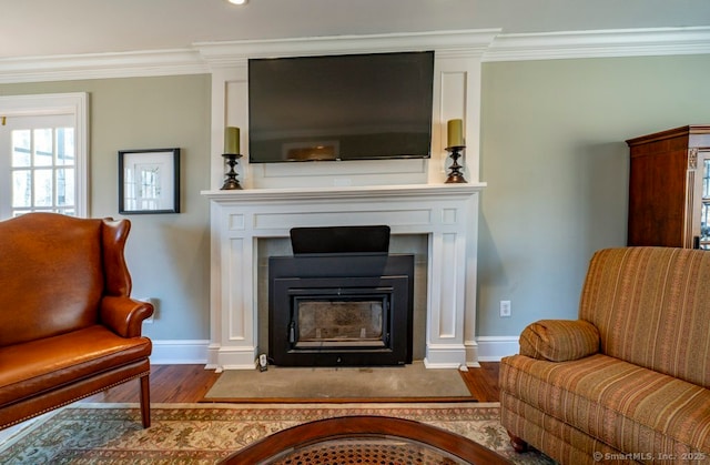 sitting room featuring baseboards, wood finished floors, ornamental molding, and a fireplace with flush hearth