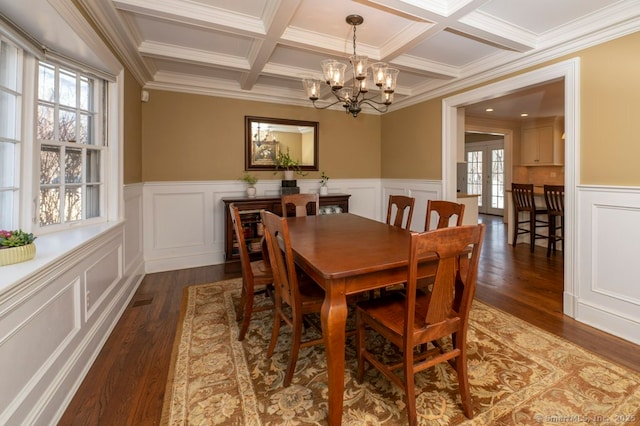 dining space with a notable chandelier, beamed ceiling, a wainscoted wall, and wood finished floors