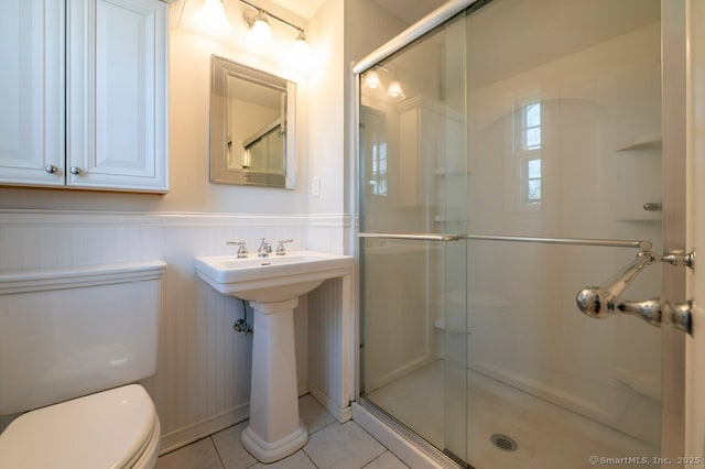 full bath with a wainscoted wall, toilet, a stall shower, and tile patterned flooring