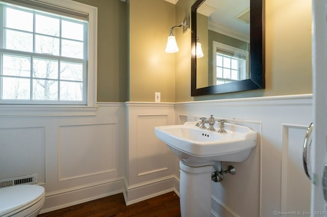 half bath featuring a wainscoted wall, toilet, a decorative wall, and wood finished floors