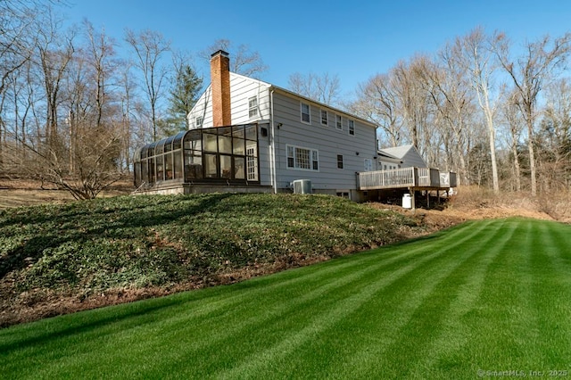 back of property with a wooden deck, a yard, a sunroom, and a chimney