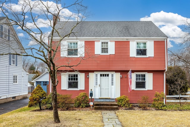 colonial home with a front yard, roof with shingles, and a chimney