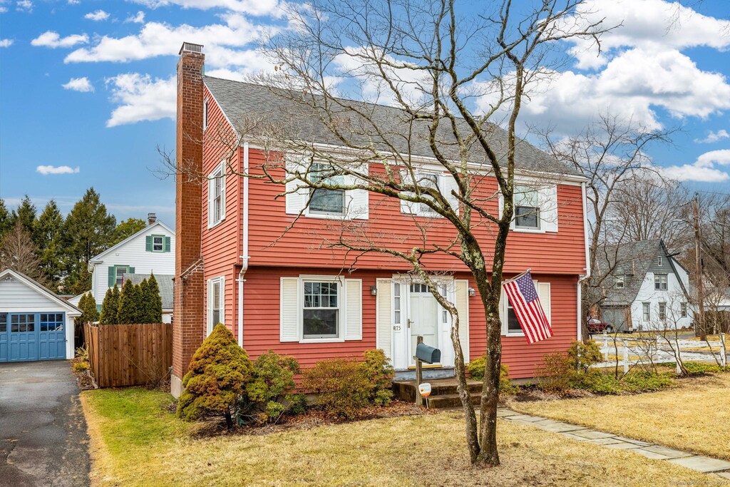 colonial house featuring driveway, a chimney, an outbuilding, fence, and a front yard