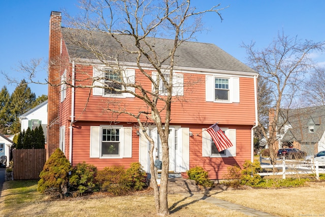 colonial-style house featuring fence, roof with shingles, and a chimney