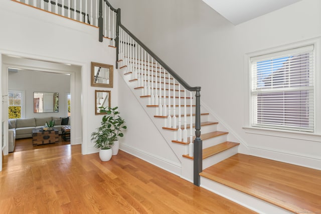 stairway featuring baseboards, a high ceiling, and wood finished floors