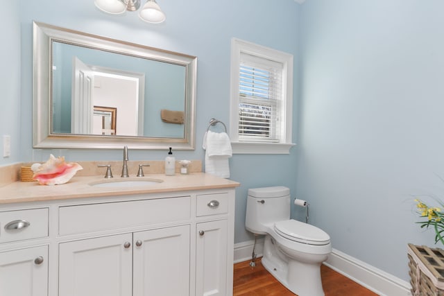 bathroom with vanity, toilet, wood finished floors, and baseboards