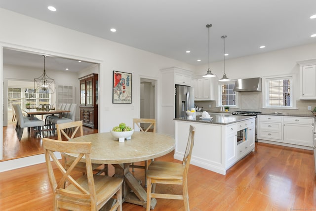 kitchen featuring wall chimney range hood, white cabinets, light wood-type flooring, and appliances with stainless steel finishes