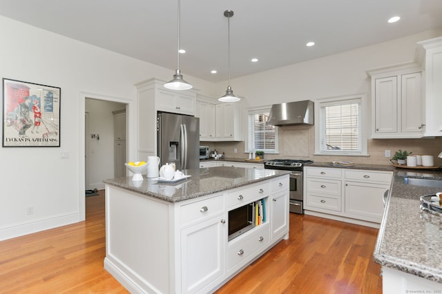 kitchen featuring light wood finished floors, a kitchen island, stainless steel appliances, white cabinetry, and wall chimney exhaust hood