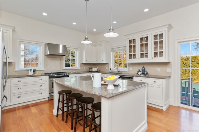 kitchen with a kitchen island, a breakfast bar, stainless steel appliances, exhaust hood, and white cabinetry