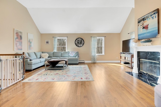 living room with baseboard heating, wood-type flooring, baseboards, and a high end fireplace