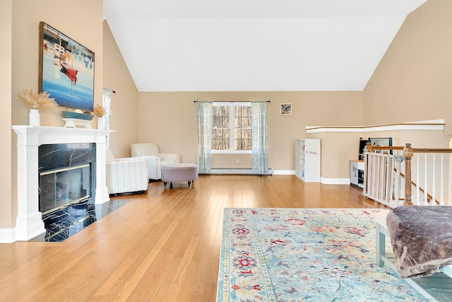 living room with wood finished floors, baseboards, lofted ceiling, a high end fireplace, and a baseboard heating unit