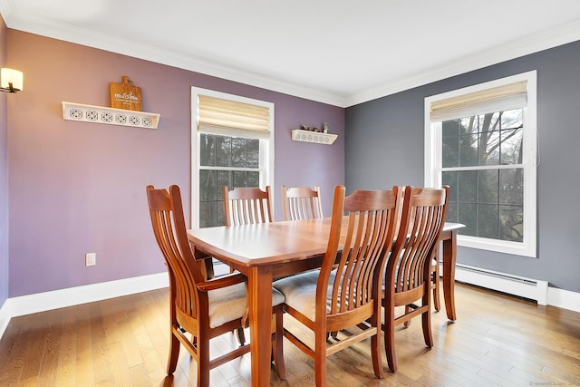 dining space featuring light wood finished floors, a healthy amount of sunlight, crown molding, and a baseboard heating unit