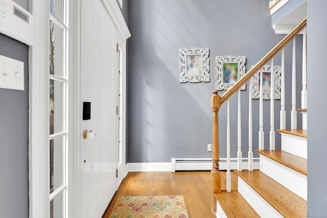 entrance foyer with stairway, a baseboard heating unit, baseboards, and wood finished floors