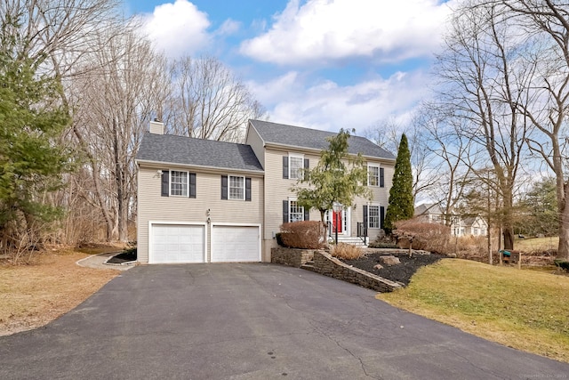 colonial house with an attached garage, a shingled roof, a front yard, a chimney, and driveway