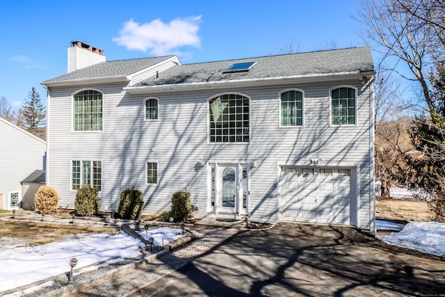 colonial home with driveway, a chimney, a garage, and a shingled roof