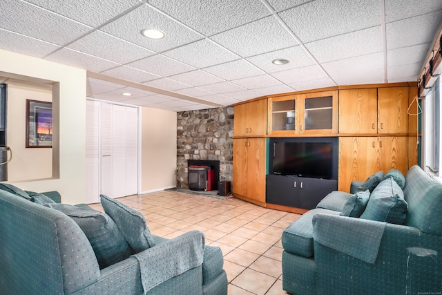 living area with light tile patterned floors, a paneled ceiling, and a stone fireplace