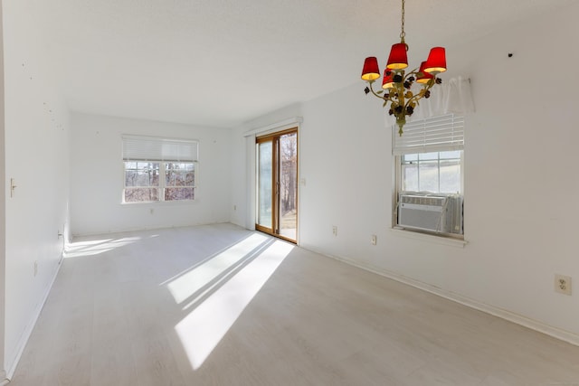 empty room featuring a notable chandelier, cooling unit, baseboards, and wood finished floors