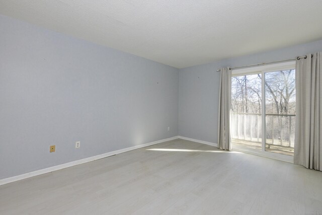 unfurnished room with a textured ceiling, baseboards, and light wood-style floors