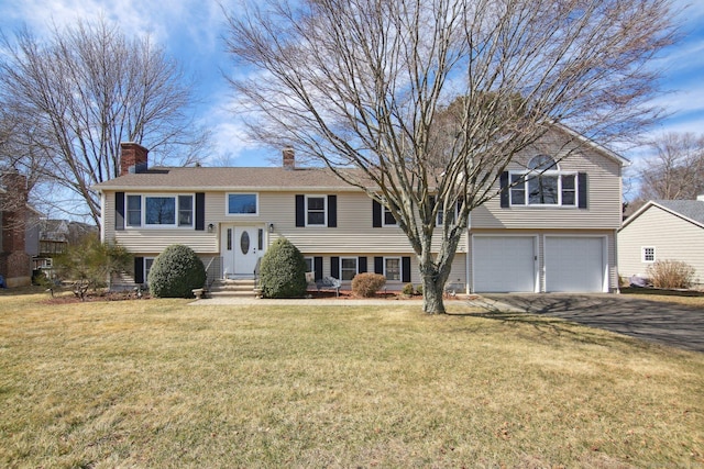 raised ranch with a front lawn, entry steps, aphalt driveway, a garage, and a chimney