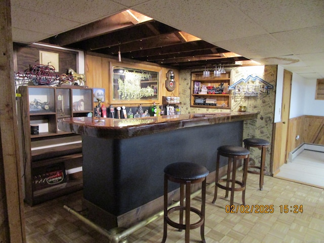 bar with a dry bar, a drop ceiling, wood walls, and wainscoting