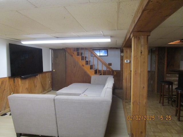 living area featuring a wainscoted wall, stairway, wood walls, a paneled ceiling, and parquet flooring