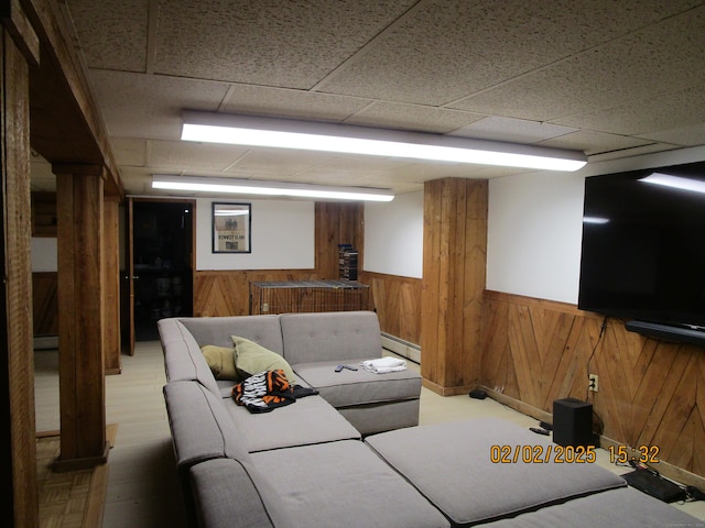 living room featuring wooden walls, a paneled ceiling, baseboard heating, and wainscoting