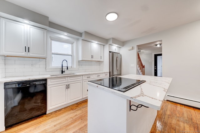 kitchen featuring light wood finished floors, light stone countertops, black dishwasher, freestanding refrigerator, and a sink