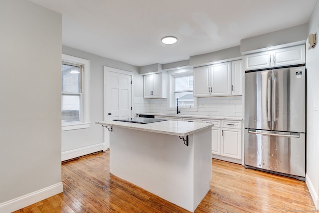 kitchen with light wood-type flooring, light stone counters, white cabinetry, freestanding refrigerator, and decorative backsplash